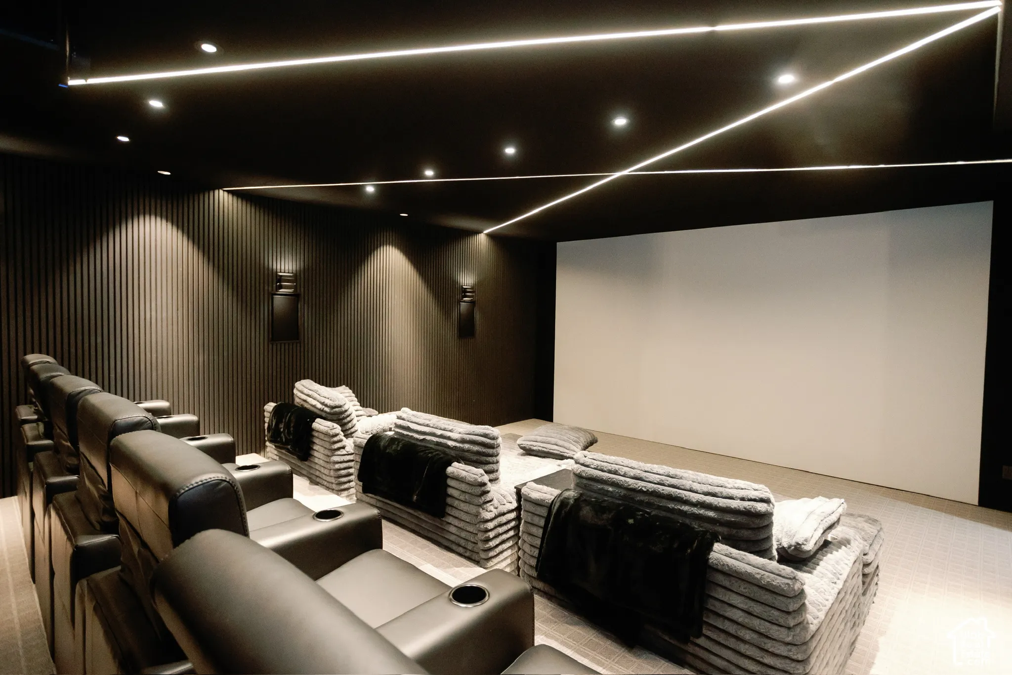 Media room featuring a recessed projection screen, vertical slat wall paneling, integrated linear ceiling lighting, and downlighting