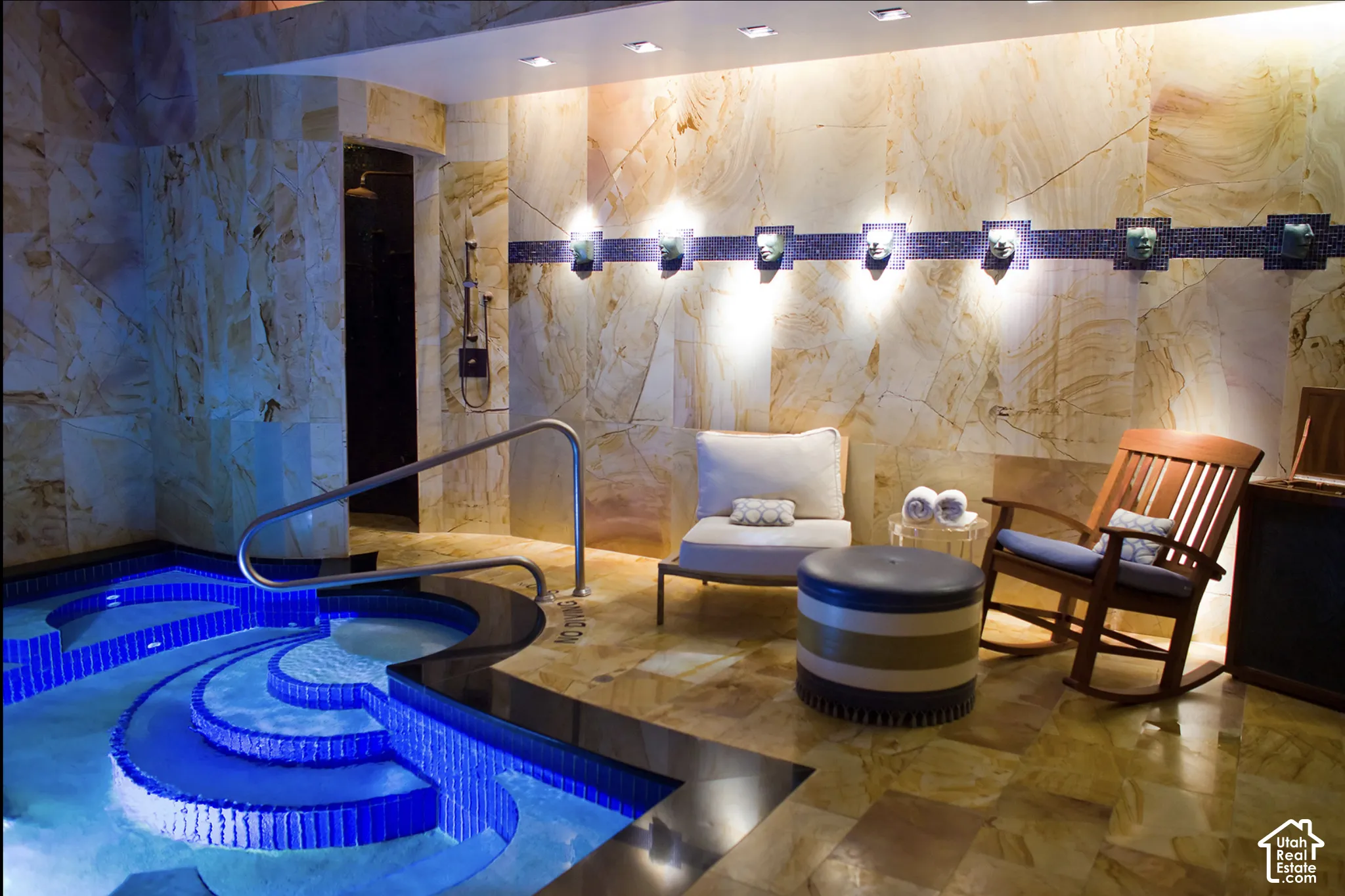 Indoor pool area featuring natural stone wall cladding, tiled pool steps, integrated recessed lighting, and a metal safety handrail