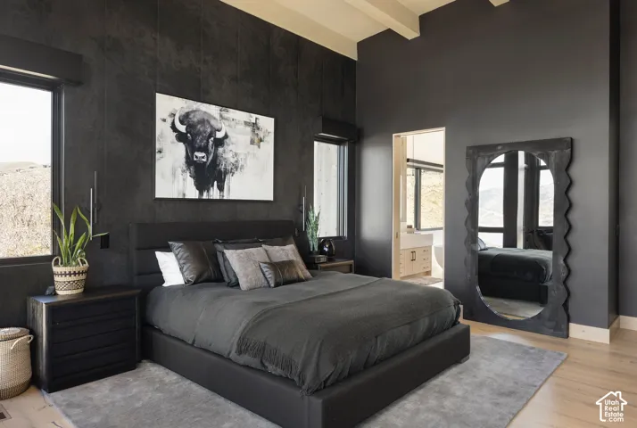 High ceilings with exposed structural beams, dark textured accent wall, vertically oriented windows, and light-toned wood-finish flooring