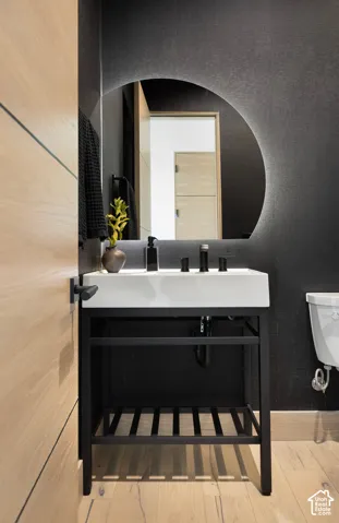 Modern vanity with a rectangular sink, black metal frame, integrated storage shelf, backlit circular mirror, and matte black widespread faucet