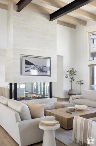 Floor-to-ceiling stone fireplace surround, double-sided glass hearth, exposed wood ceiling beams, steel structural support beams, and oversized windows