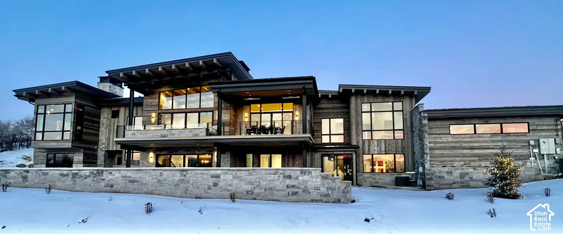 Contemporary exterior featuring wood-plank siding, natural stone accents, expansive floor-to-ceiling windows, deep roof overhangs with exposed rafters, and a tiered stone retaining wall