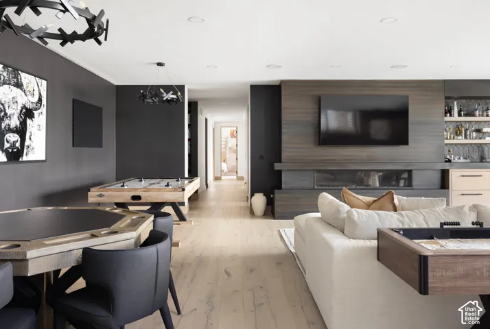 Open-concept interior featuring wood-finish flooring, a linear fireplace with horizontal wood paneling, recessed lighting, sculptural chandeliers, and built-in bar cabinetry