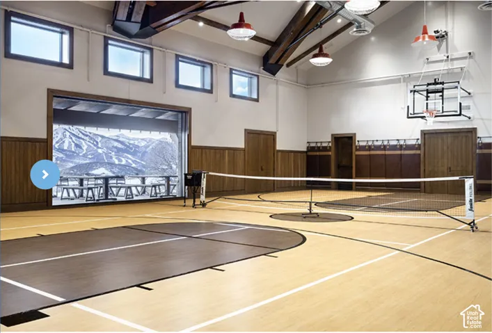 Indoor sports court featuring high vaulted ceilings, wood-finish wall paneling, a wall-mounted basketball hoop, overhead pendant lighting, and mountain scenery