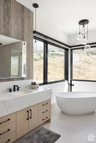Modern bathroom featuring wood-panel accent walling, white quartz countertops, light wood cabinetry with matte black hardware, a freestanding soaking tub, and floor-to-ceiling windows with black framing