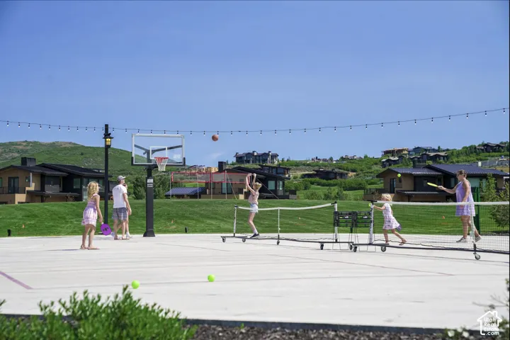 Concrete sport court featuring a basketball hoop, overhead string lighting, and painted court lines
