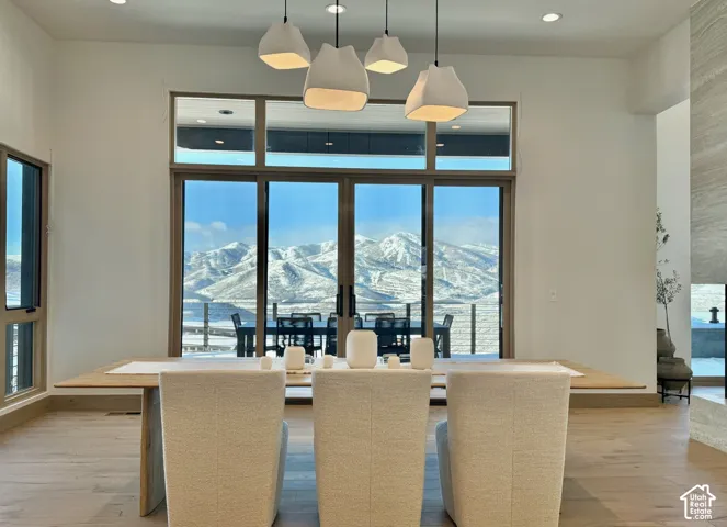 Open-concept interior featuring wood-finish flooring, multi-pendant lighting, sliding glass door with transom window, and mountain backdrop