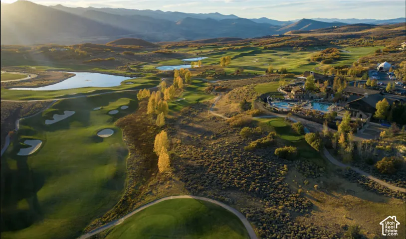 Aerial landscape featuring expansive golf course fairways, water hazards, mature trees, and a mountain backdrop
