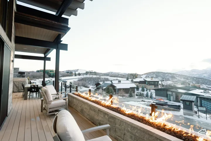 Covered deck featuring composite decking, linear built-in gas fire feature with stone masonry surround, and metal cable railing