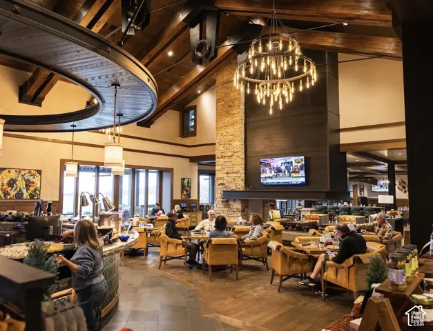 Vaulted ceiling with exposed wood beams, full-height stone fireplace, multi-tier circular chandelier, and wood-finish flooring