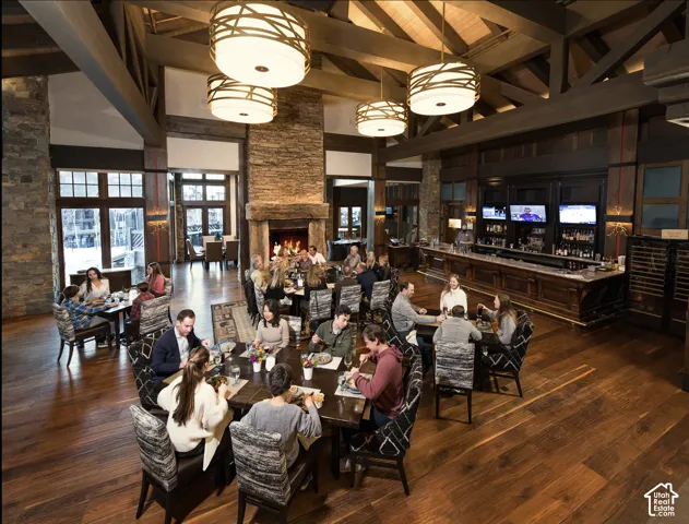 Exposed timber trusses, floor-to-ceiling stone fireplace, wide-plank wood-finish flooring, custom wood bar cabinetry, and drum-style pendant lighting