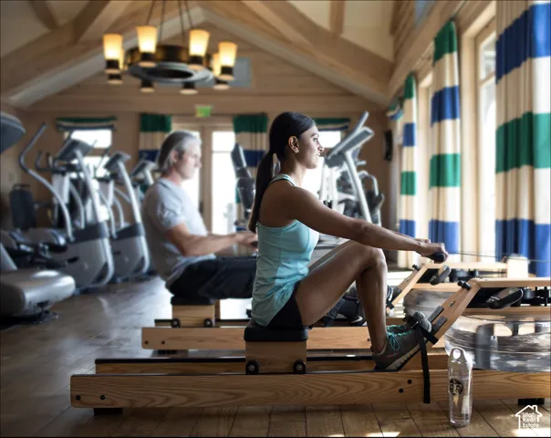 Fitness facility featuring a vaulted ceiling with exposed timber beams, wood-finish flooring, and a multi-arm chandelier