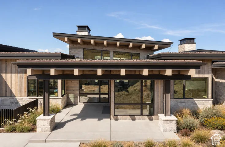 Contemporary architectural exterior featuring wood siding, stone masonry, a shed roofline with exposed rafter tails, and expansive multi-pane windows