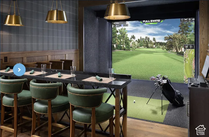 Golf simulator room featuring an integrated projection screen, high-top bar with dark stone countertop, wood wainscoting, and metallic pendant lighting