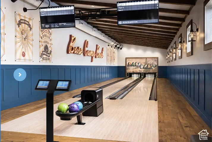 Private bowling alley featuring dual synthetic lanes, custom overhead digital scoring monitors, wood-finish flooring, and wall-mounted sconce lighting against wainscoting-paneled walls