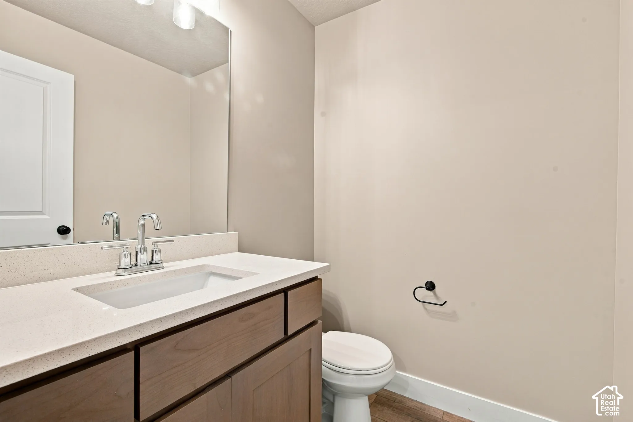 Vanity featuring a stone-composite countertop with an integrated rectangular sink, wood-finish cabinetry, a large wall-mounted mirror, and a chrome faucet fixture