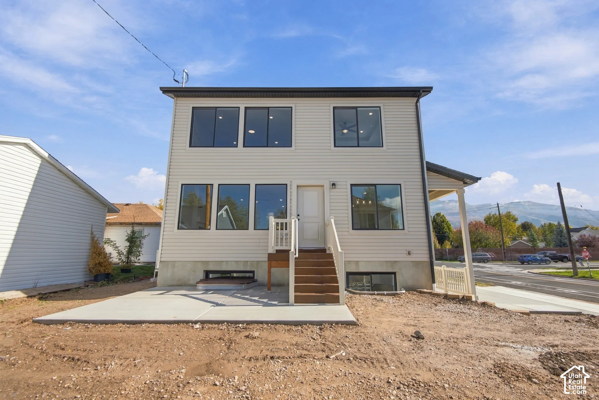 Two-story exterior featuring horizontal siding, a poured concrete patio, a wooden staircase with railing, and large multi-pane windows
