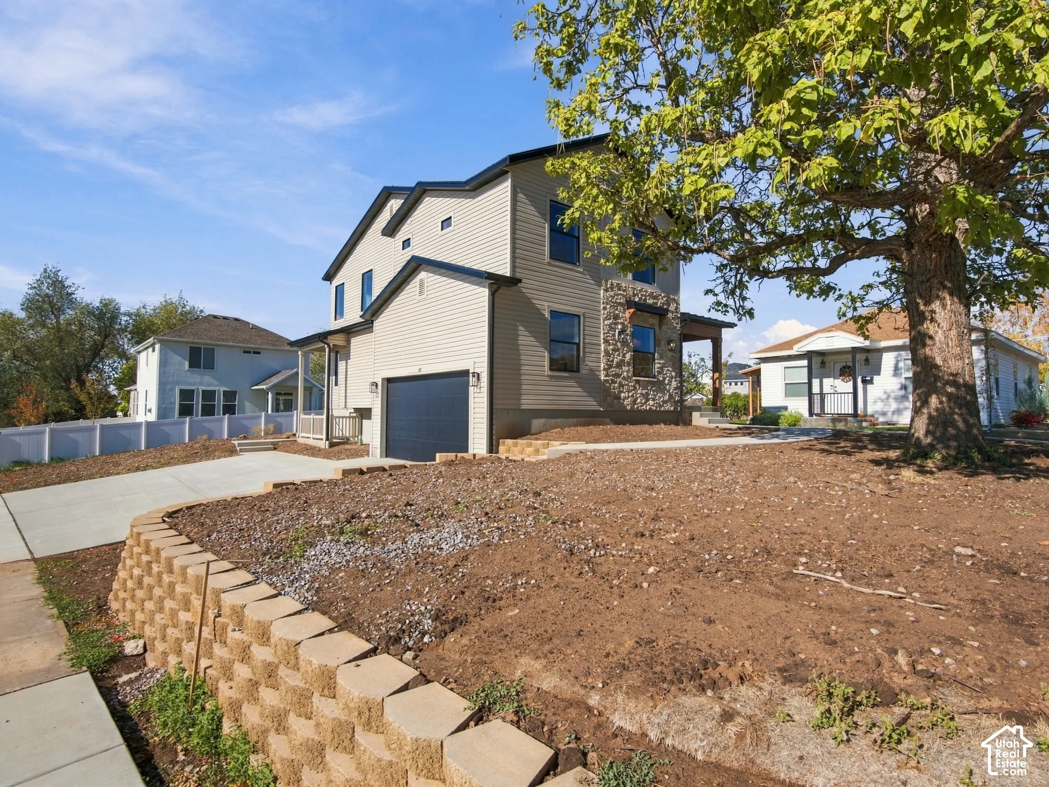 Two-story residence featuring light-toned horizontal siding, a stone veneer facade, a dark-finished single-car garage, and a tiered concrete retaining wall