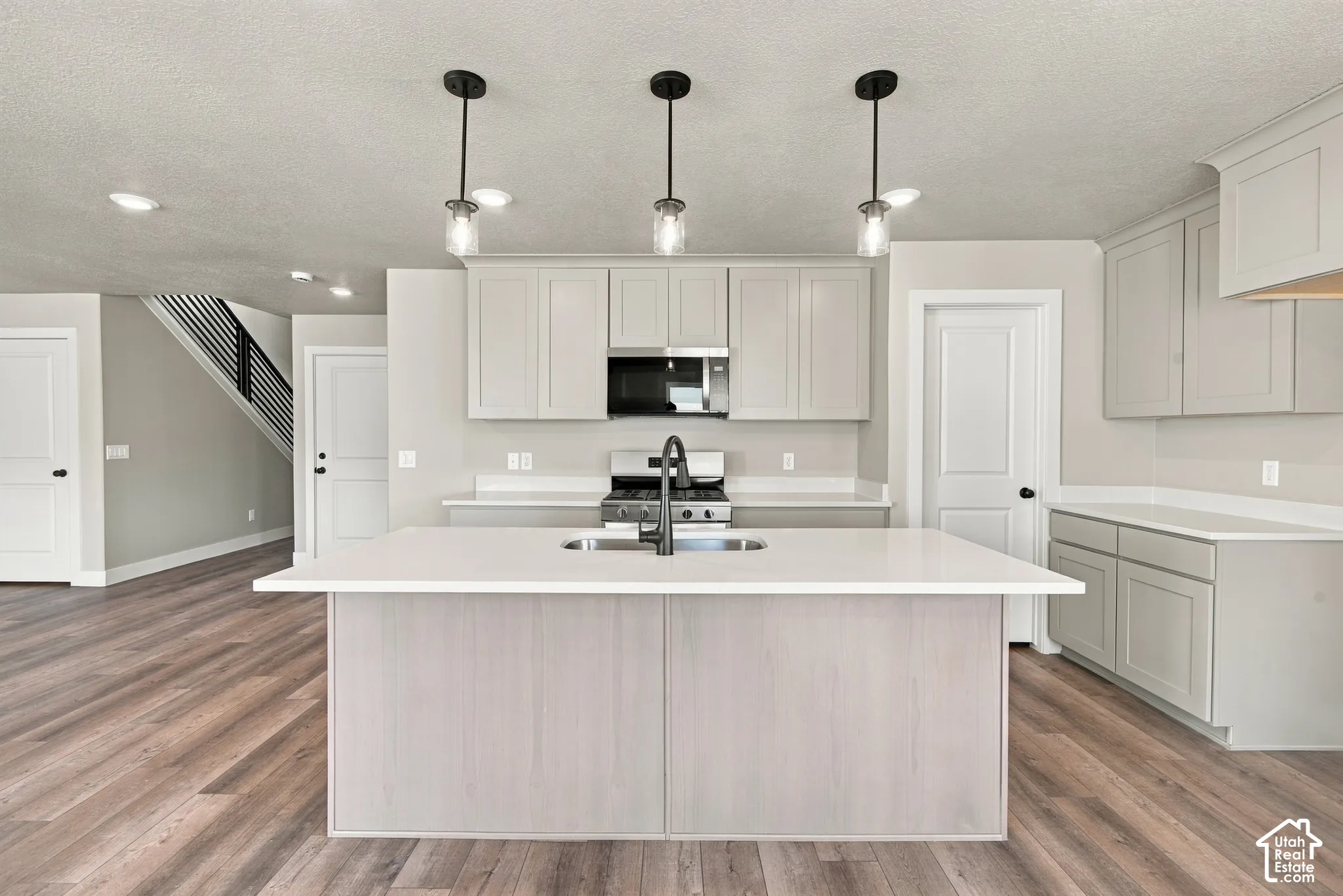 Kitchen featuring a center island with solid-surface countertops, shaker-style cabinetry, stainless steel appliances, wood-finish flooring, and pendant lighting