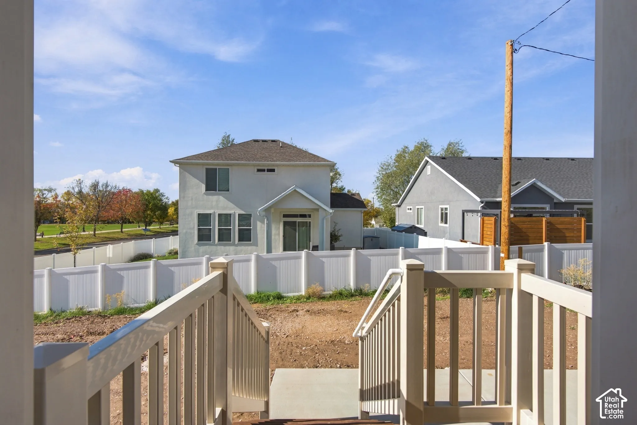 Elevated composite deck featuring white railings and stairs with direct access to a concrete patio and enclosed rear yard with white vinyl fencing