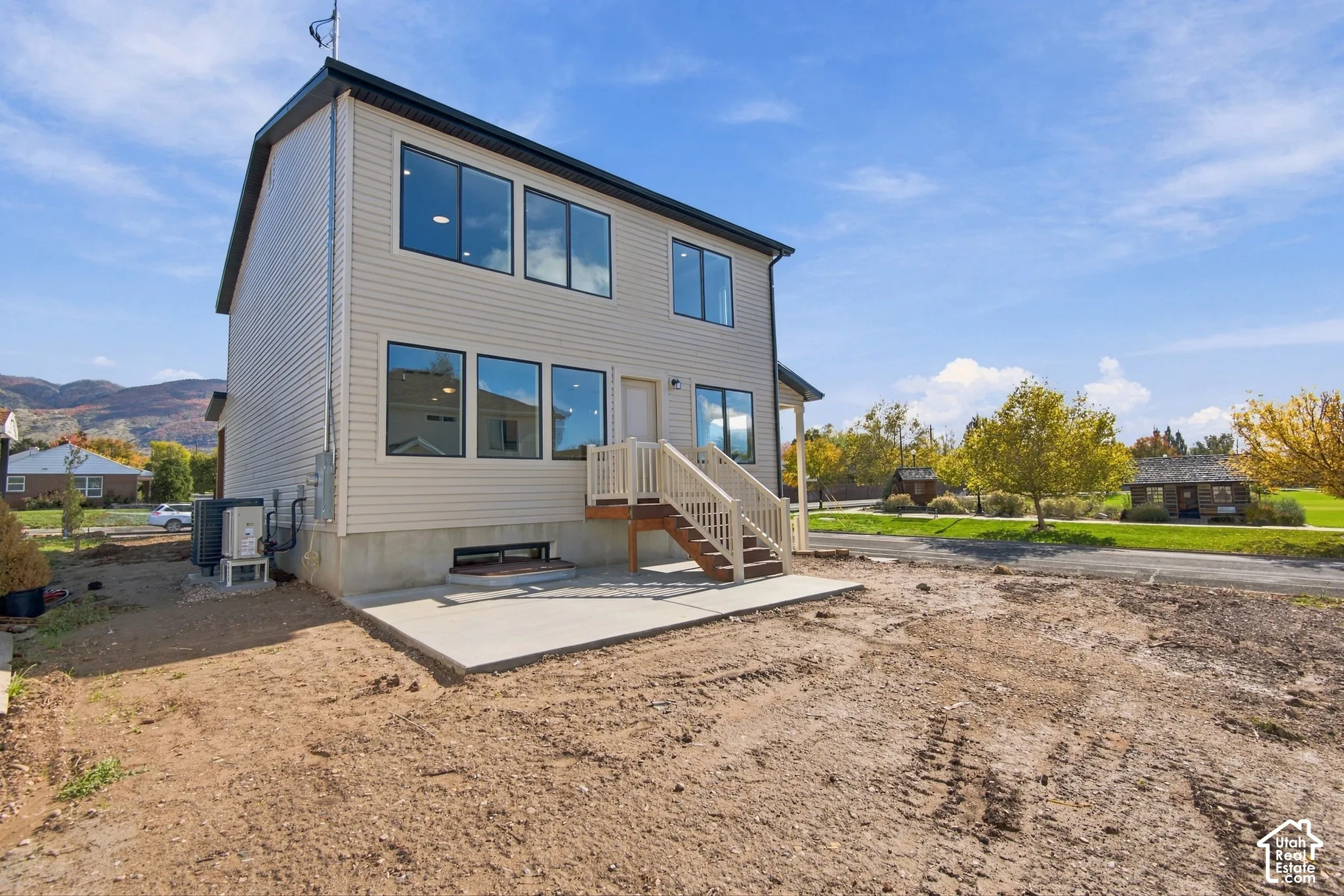 Two-story residence featuring light-colored horizontal siding, large picture windows, a concrete patio, and a wood-frame deck with balusters