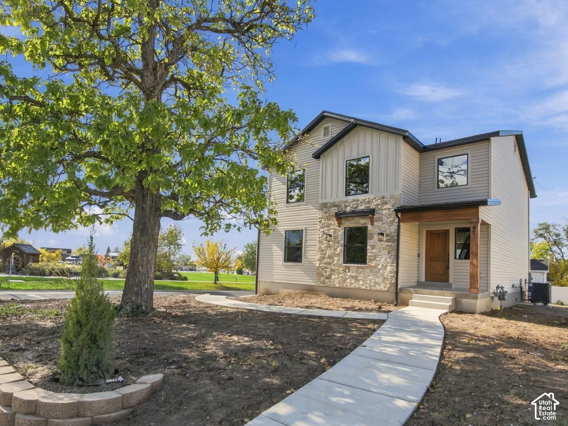 Two-story exterior featuring composite siding, stone veneer accents, a covered front porch with wood-finished support columns, and a segmental retaining wall