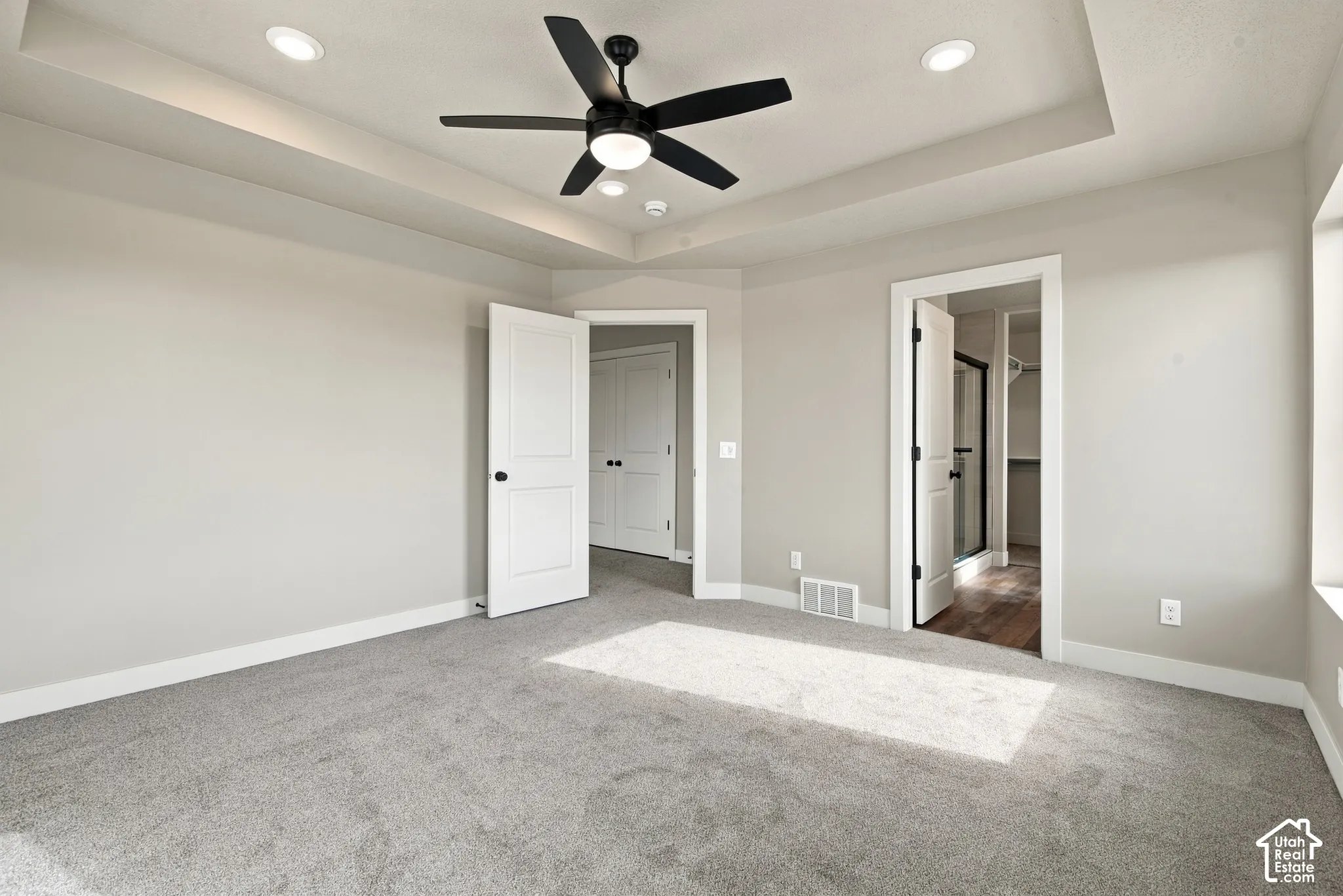 Tray ceiling with recessed lighting and a central matte black ceiling fan, complemented by neutral wall paint, plush carpeting, and two-panel interior doors