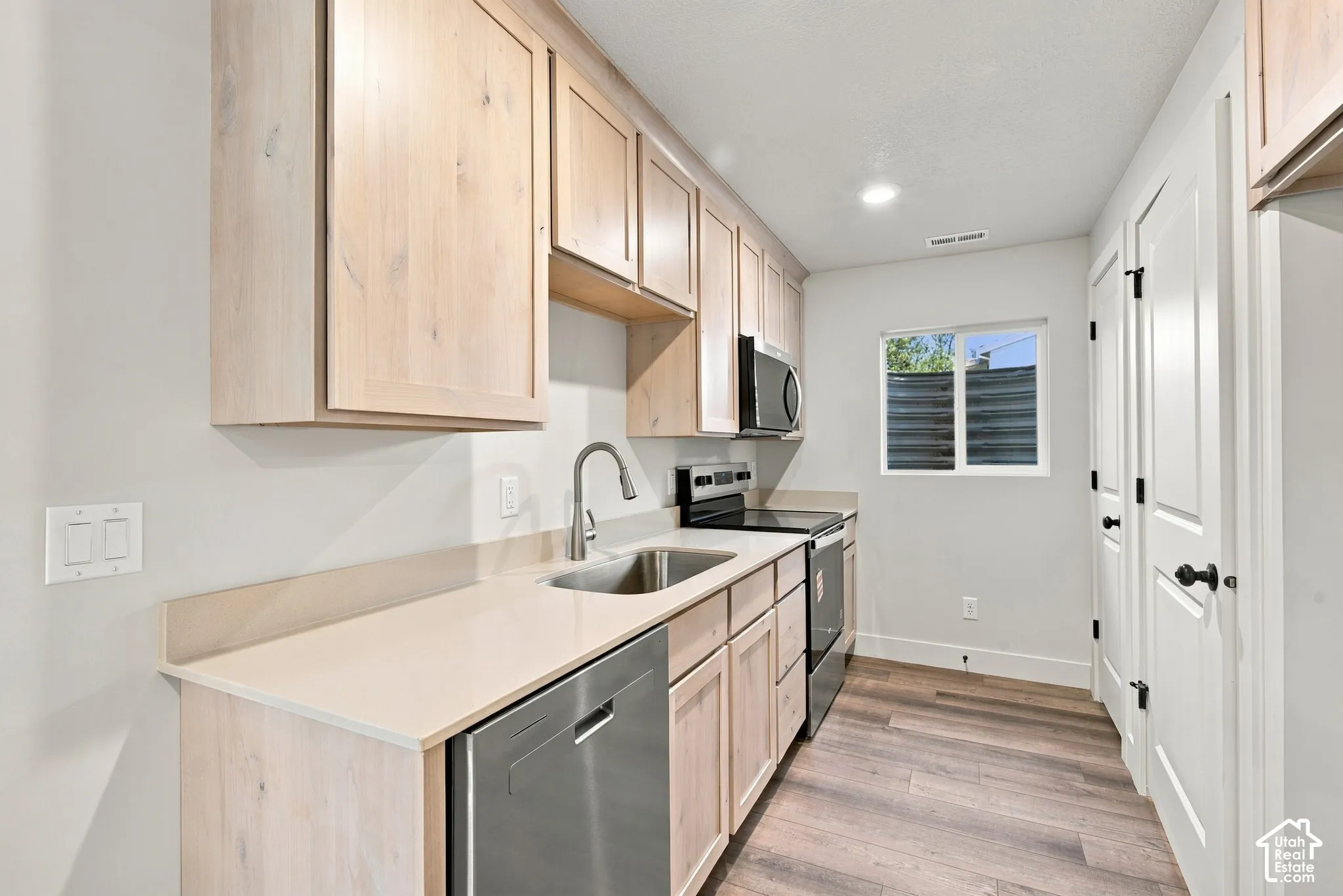 Kitchen featuring light wood-finish cabinetry, solid-surface countertops, stainless steel appliances, and wood-finish flooring