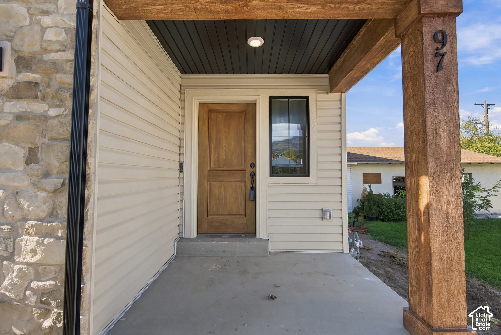 Covered entryway featuring a wood-finish front door, stone veneer siding, horizontal lap siding, recessed lighting, and a timber-finish support column