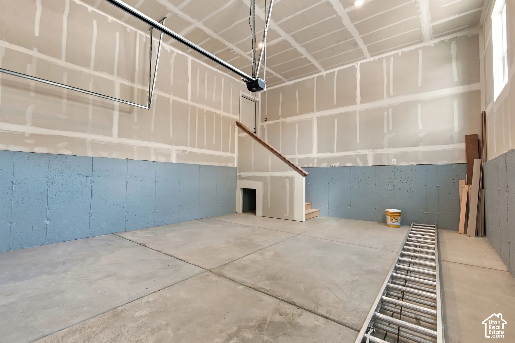 Spacious garage with high ceilings, concrete flooring, painted masonry lower walls, and integrated stairwell