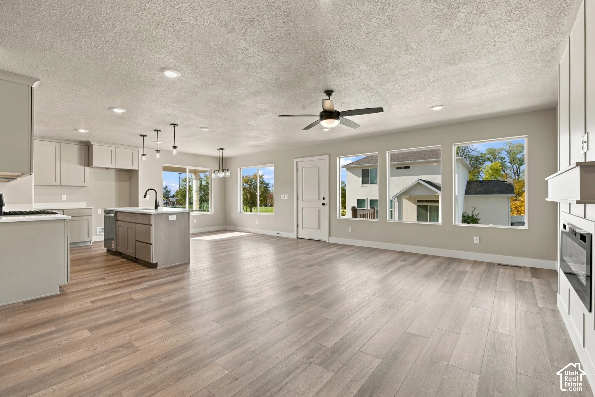 Open-concept space featuring wood-finish flooring, a kitchen island with a matte black faucet, recessed lighting, a ceiling fan, and a built-in electric fireplace