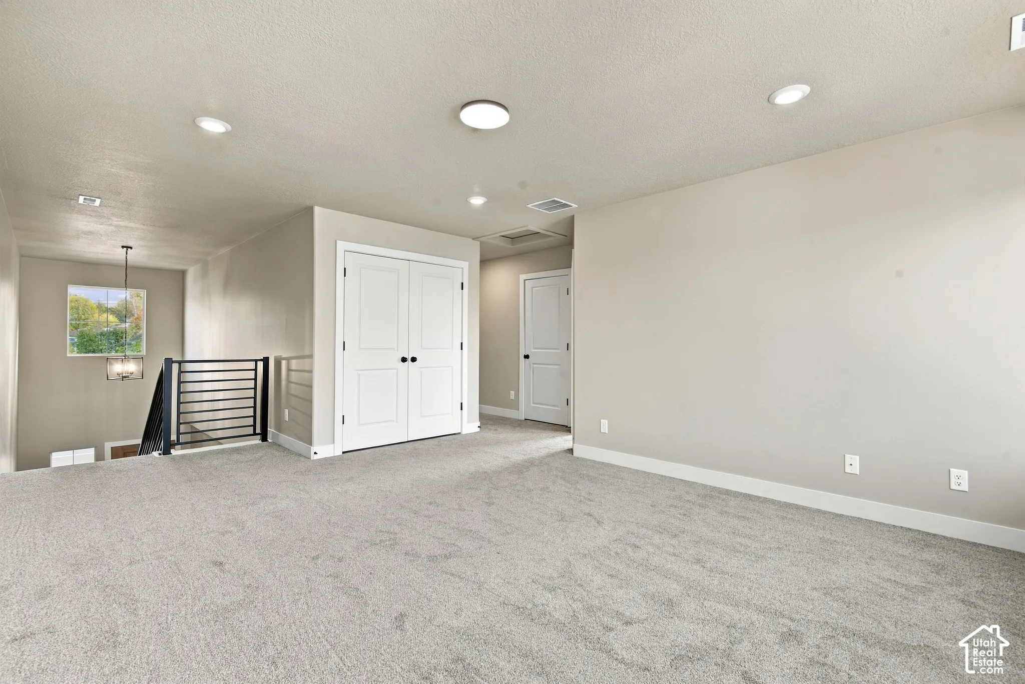 Neutral-toned interior space featuring recessed ceiling lighting, wall-to-wall carpeting, metal stair railing, and dual-panel closet doors