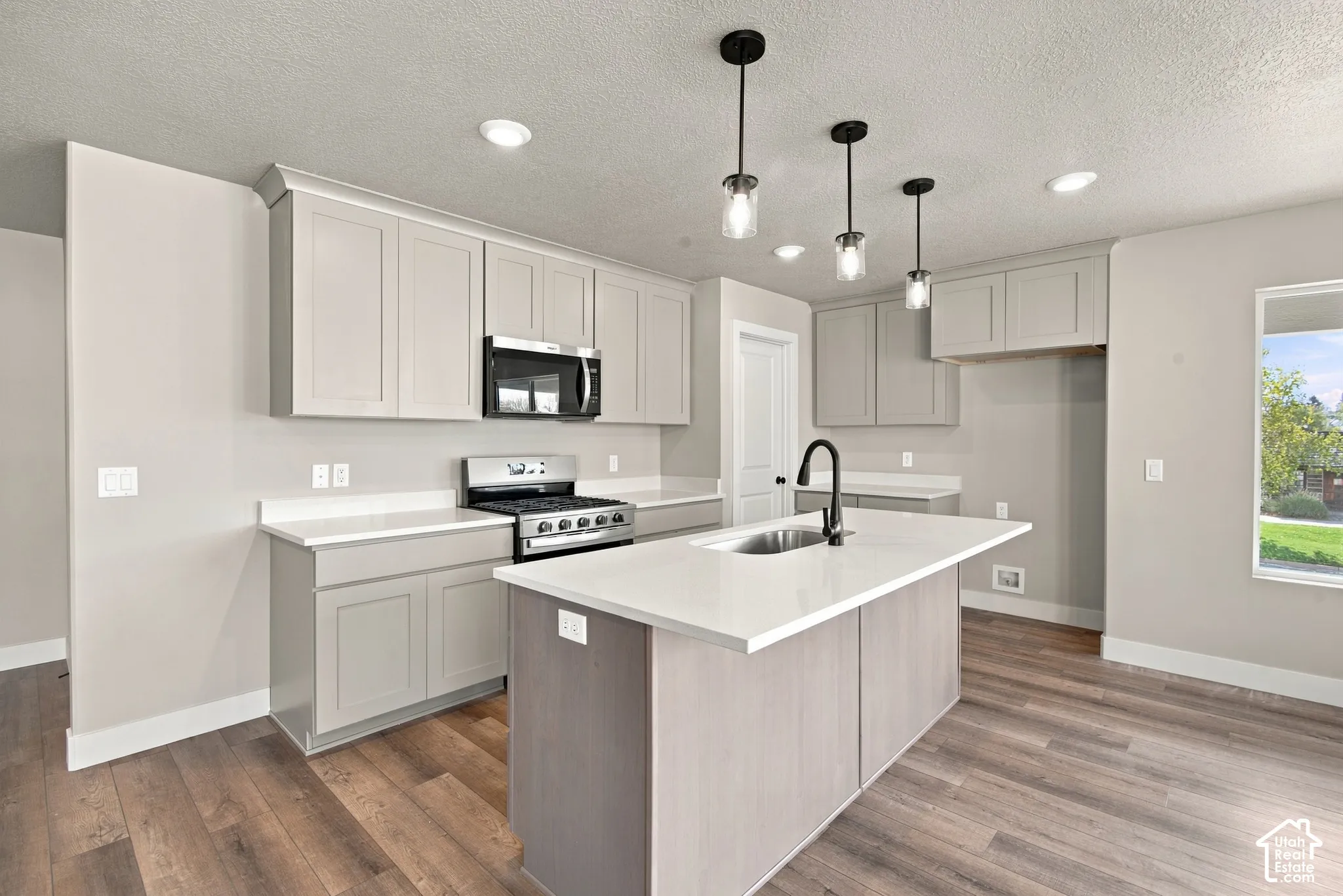 Kitchen featuring a center island with a stone-surface countertop, shaker-style cabinetry, stainless steel range and microwave, recessed lighting, and wood-finish flooring