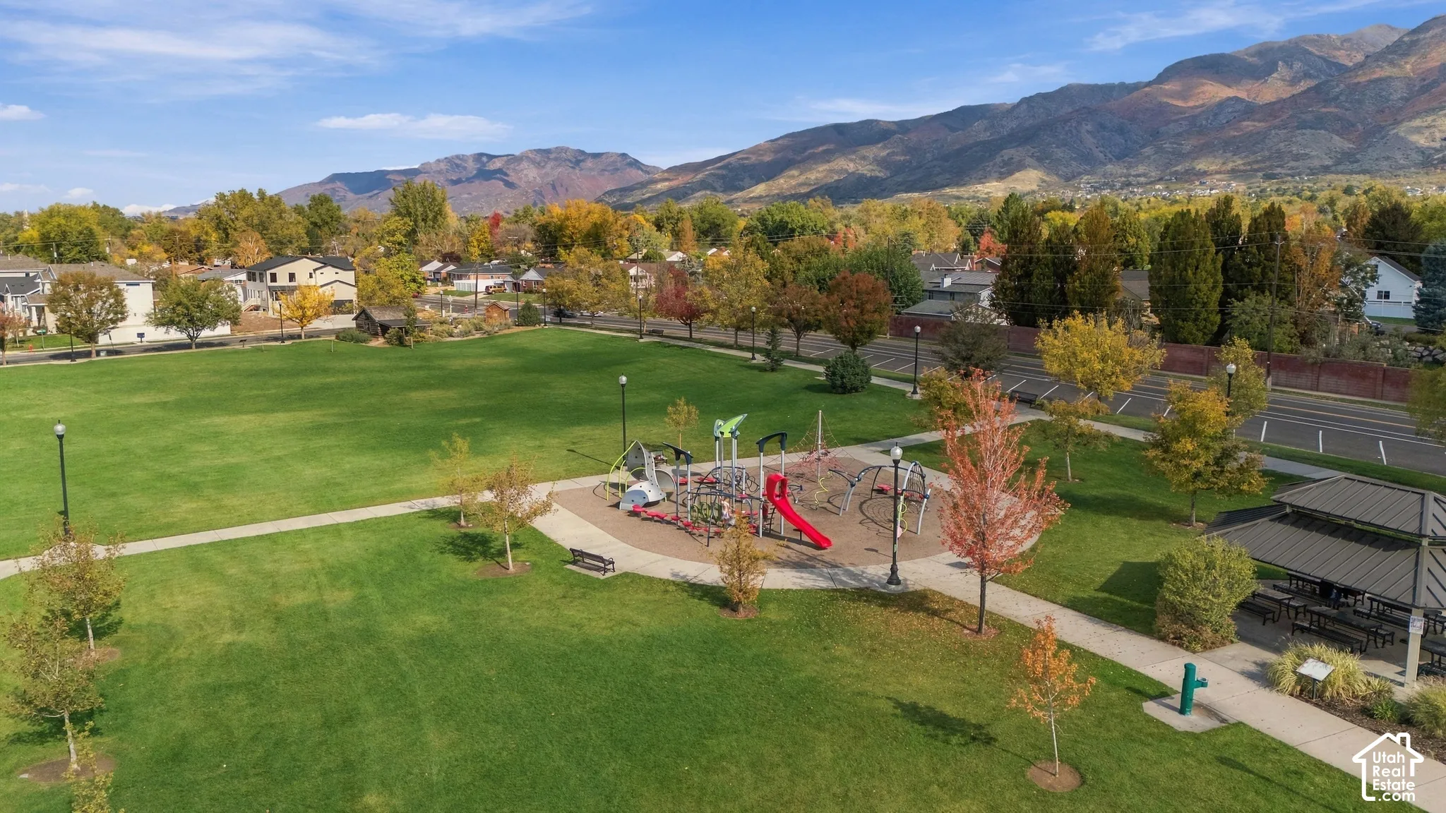Expansive green space featuring a playground with a slide, pedestrian walkways, a covered pavilion, and mountain scenery