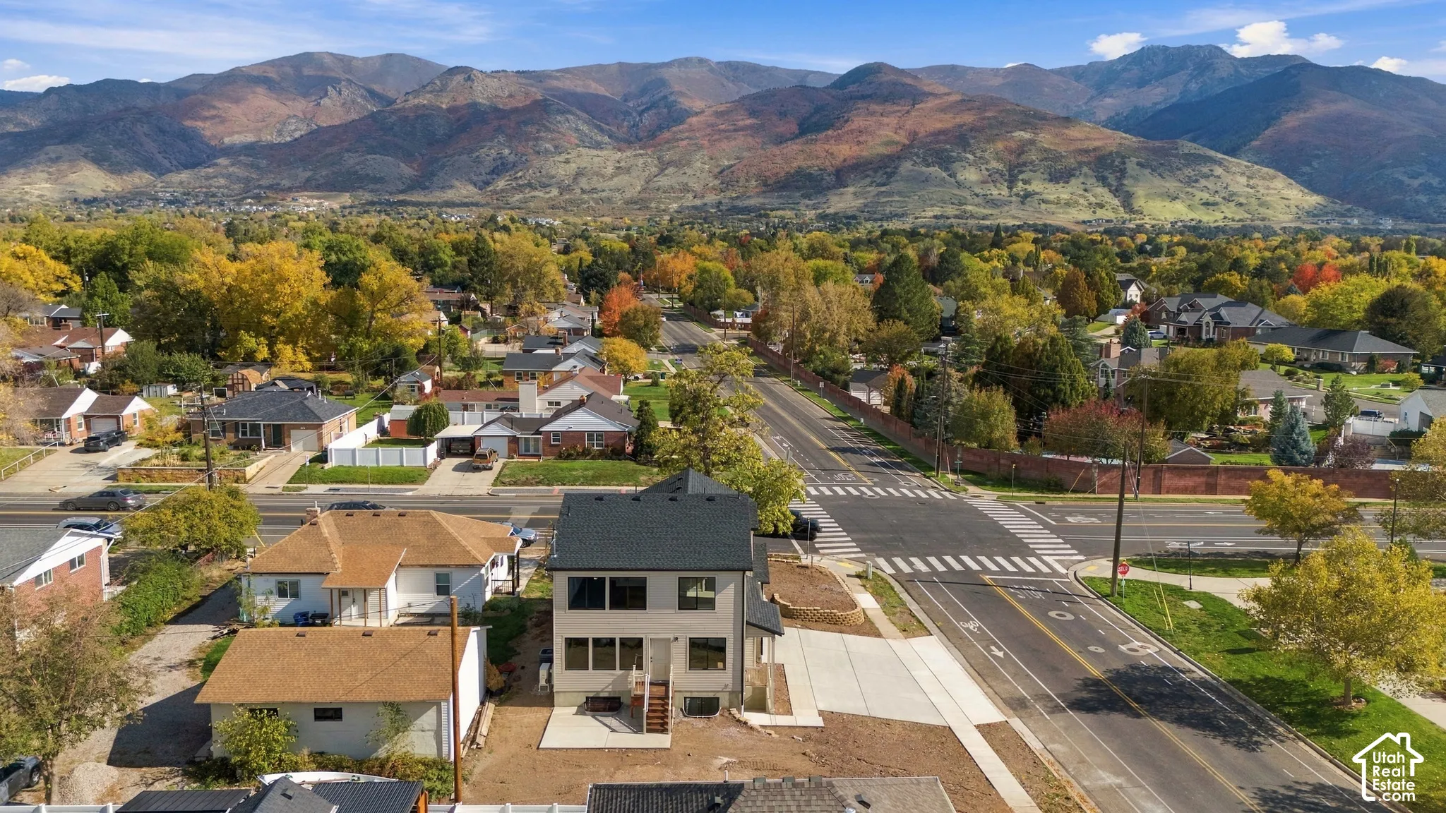 Two-story exterior with a multi-gabled roofline, light-toned siding, tiered rear concrete patio, and a mountain backdrop
