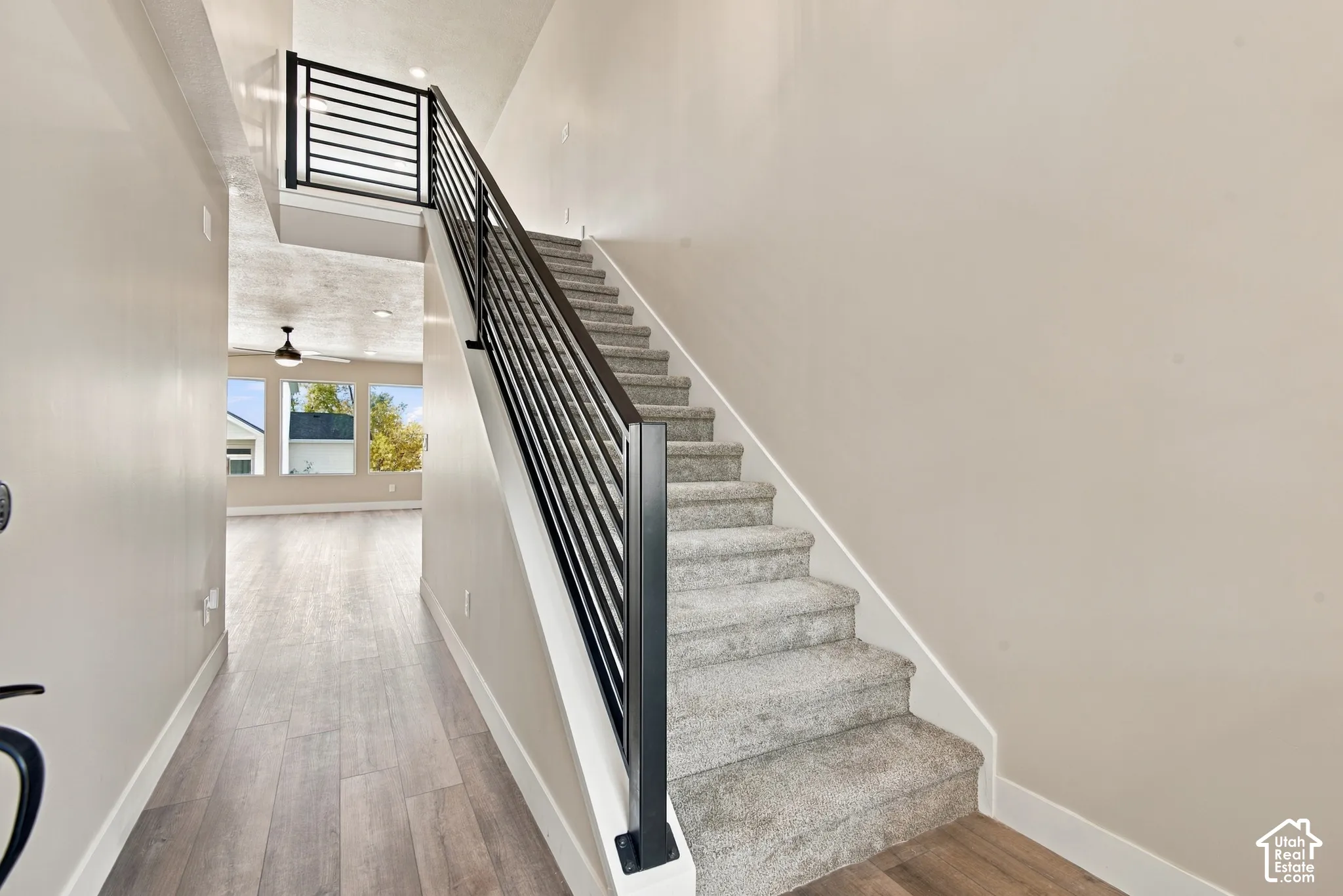 Staircase featuring a matte black horizontal-bar railing, neutral carpeting, and wood-finish flooring