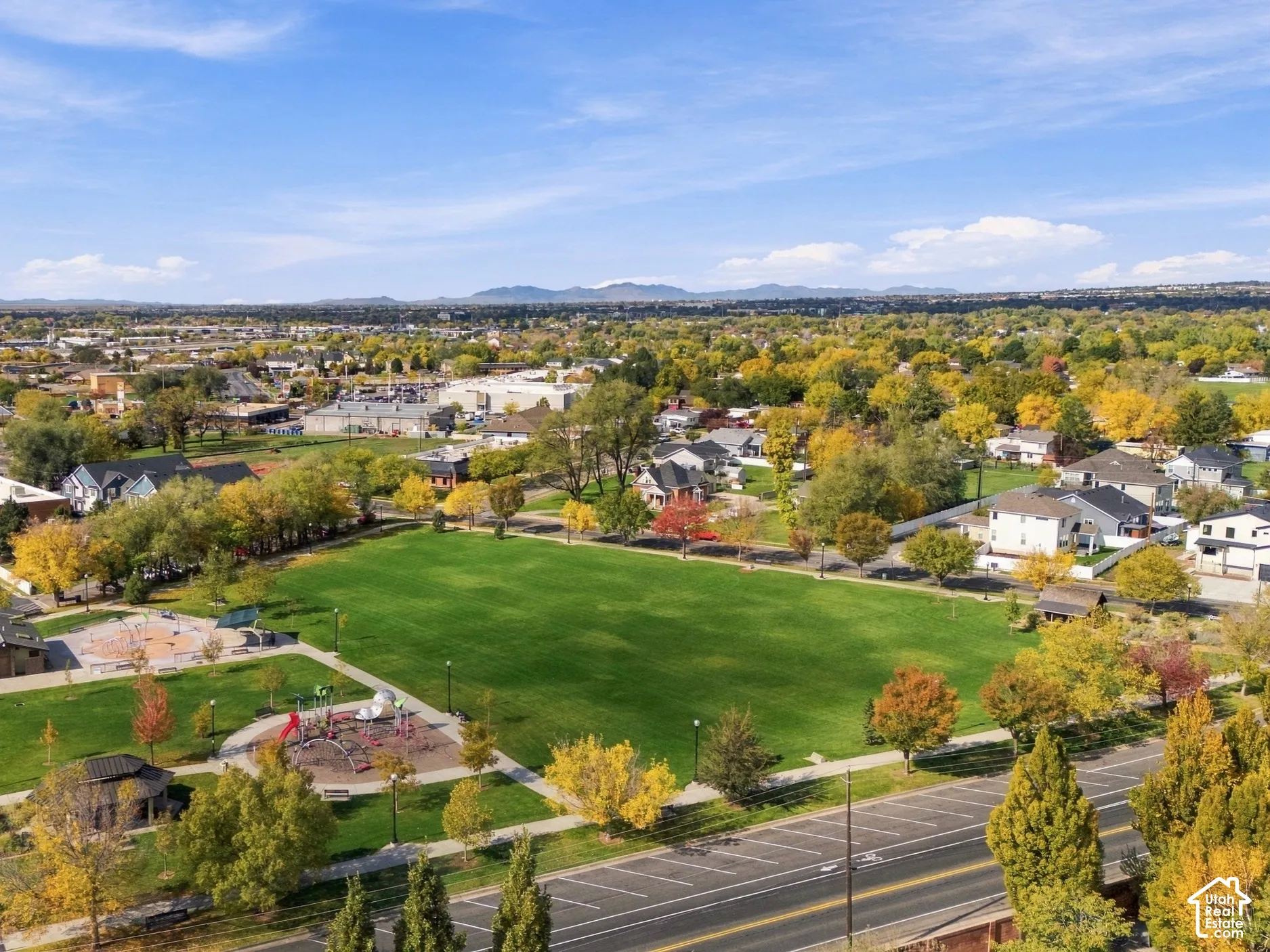 Aerial perspective of an expansive public park featuring a large manicured lawn, paved walkways, and playground structures