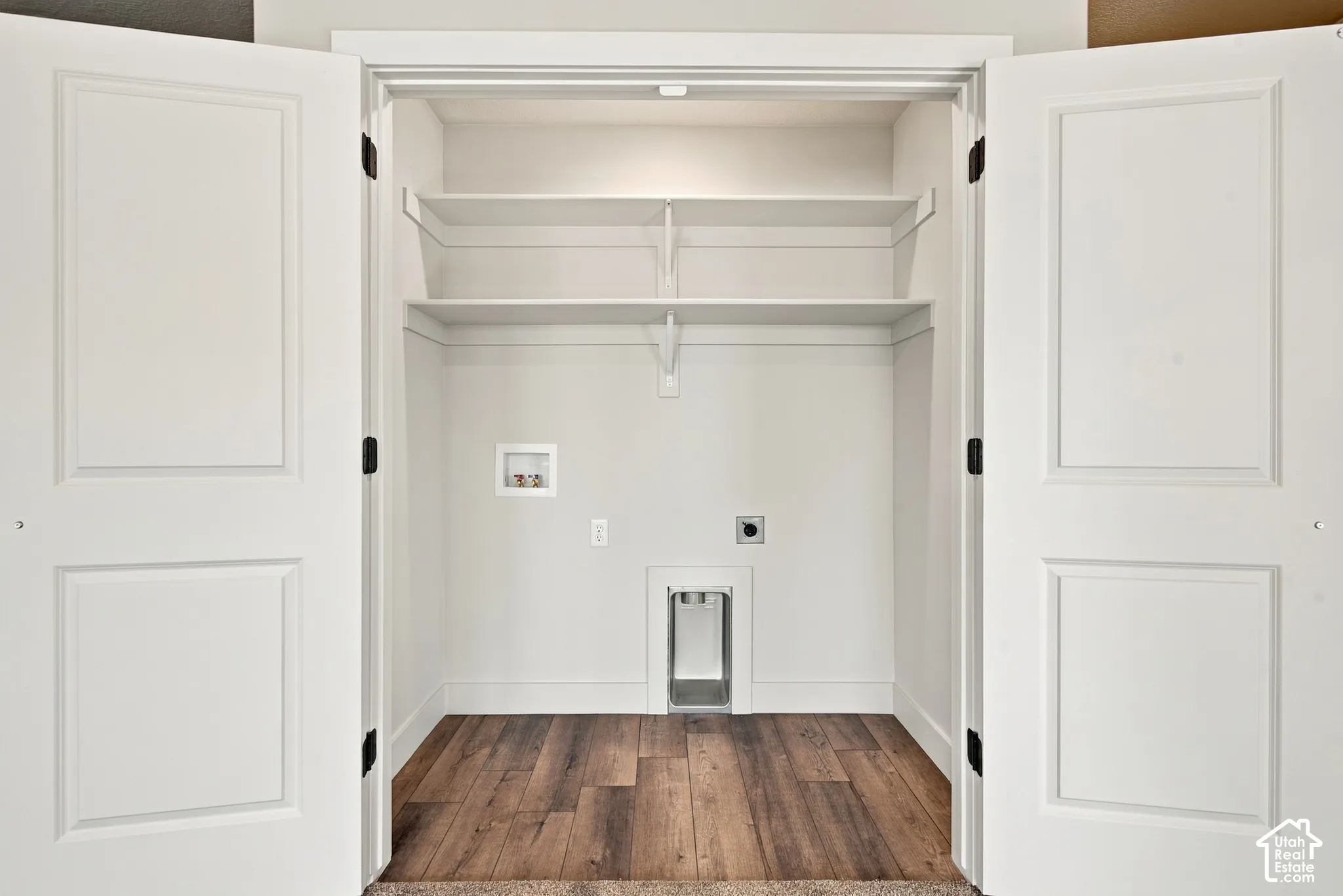 Utility closet featuring double panel doors, wood-finish flooring, two tiers of built-in shelving, and recessed laundry hookups