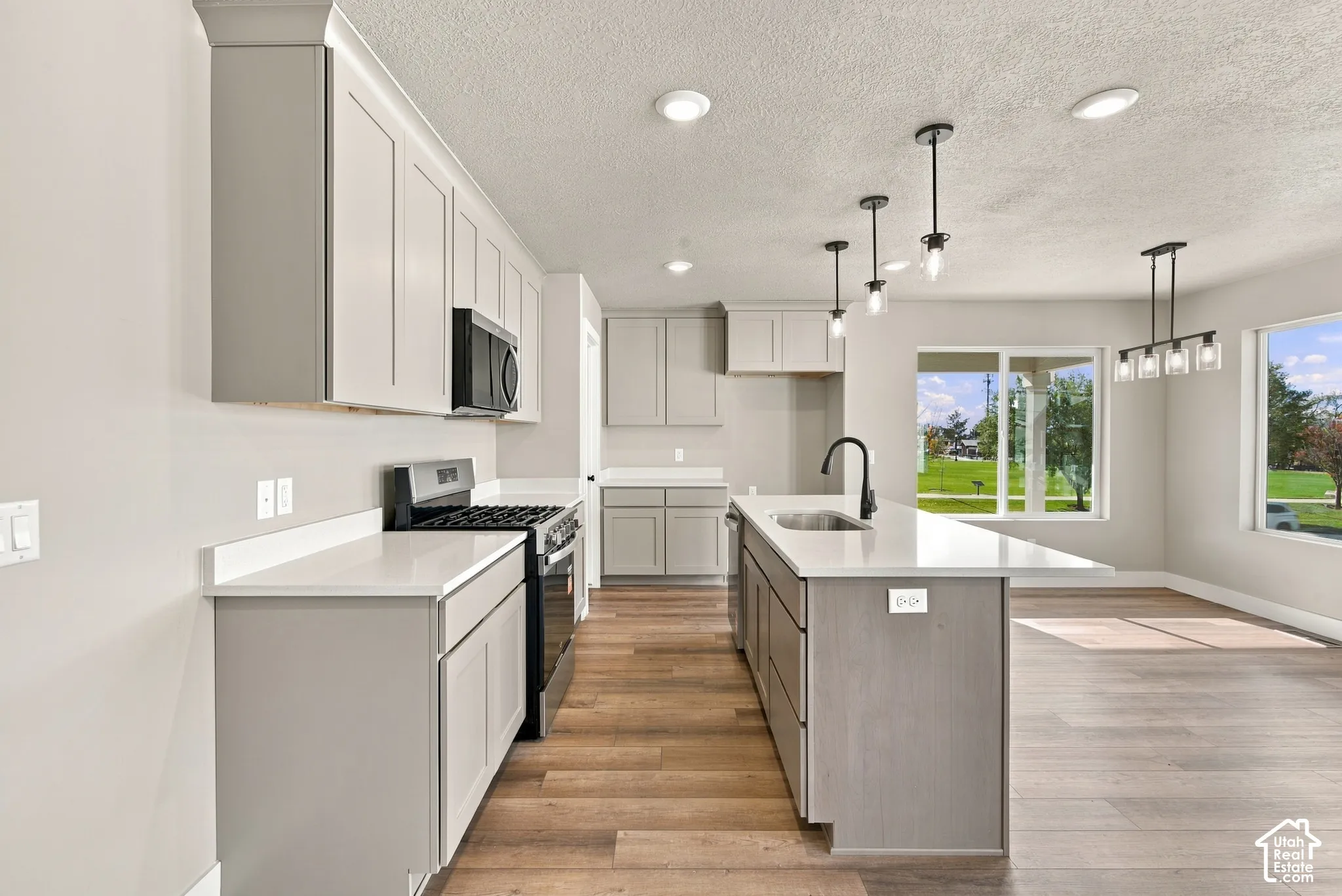 Kitchen featuring shaker-style cabinetry, quartz countertops, a central island with an undermount sink and matte black faucet, and wood-finish flooring