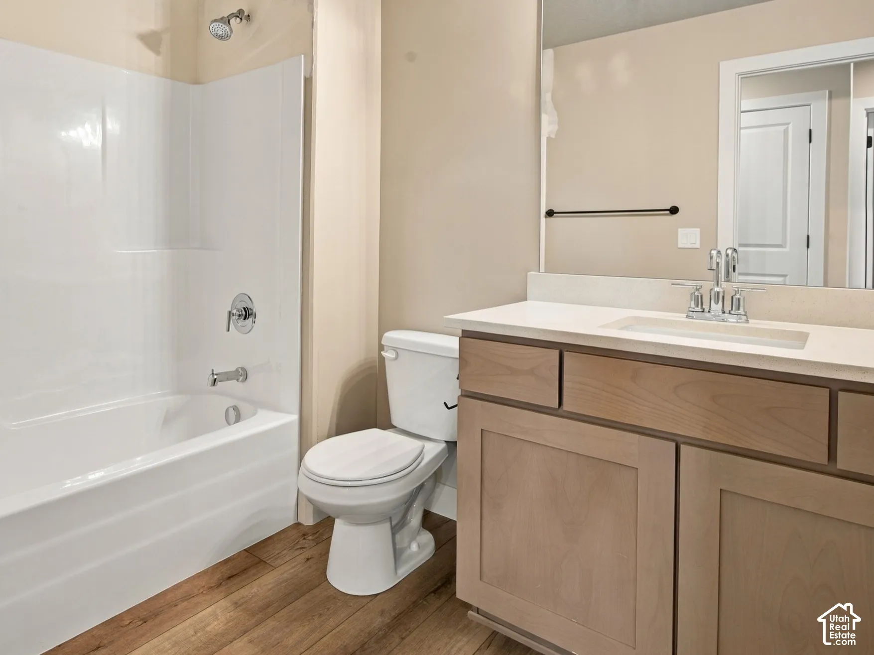 Bathroom featuring a light wood-finish vanity, solid-surface countertop with an integrated sink, wood-finish flooring, white tub-shower combination, and a multi-light fixture