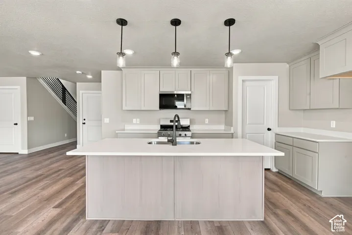 Kitchen featuring a center island with solid-surface countertops, shaker-style cabinetry, stainless steel appliances, wood-finish flooring, and pendant lighting