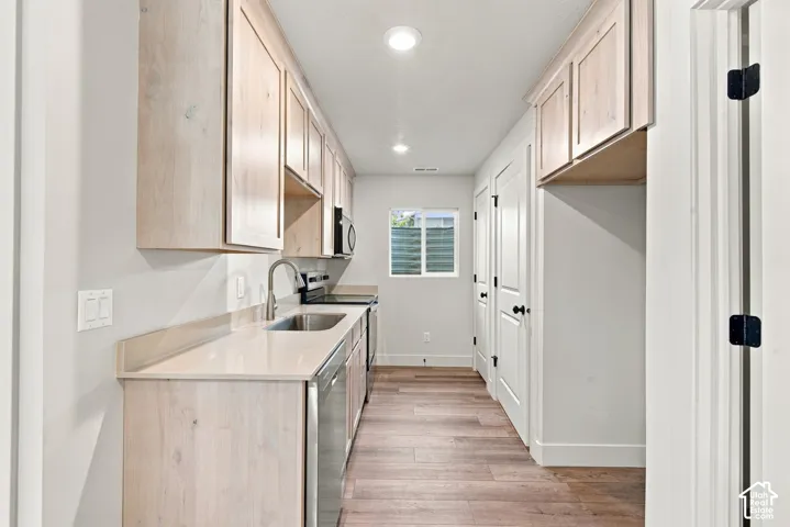 Galley kitchen featuring light-toned wood-finish cabinetry, solid surface countertops, stainless steel appliances, and wood-finish flooring