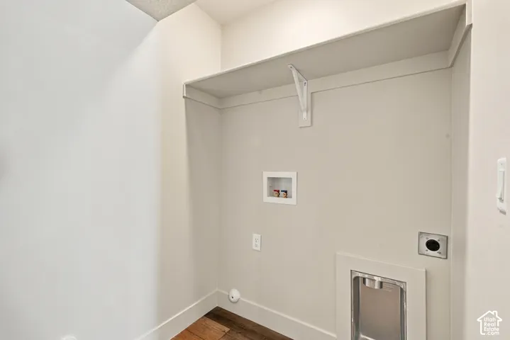 Utility area featuring wood-finish flooring, a white overhead storage shelf with bracket support, and recessed water and dryer hookups