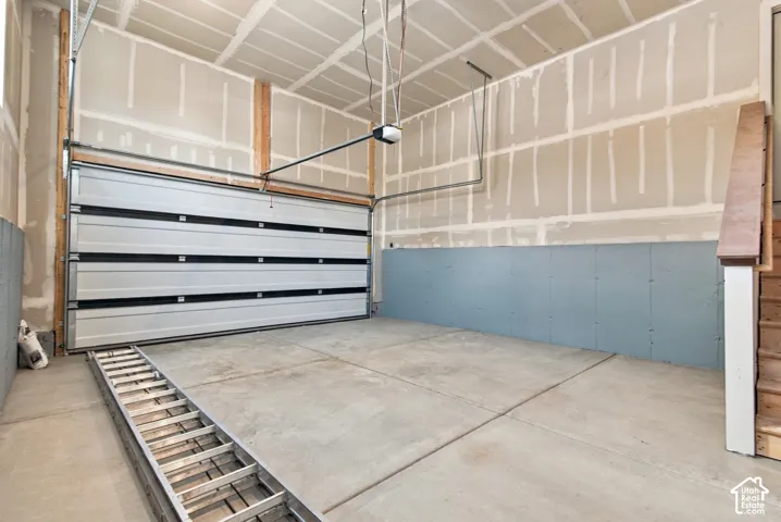 Attached garage featuring a multi-panel overhead door, concrete flooring, high ceilings, and interior stairs with a wooden handrail