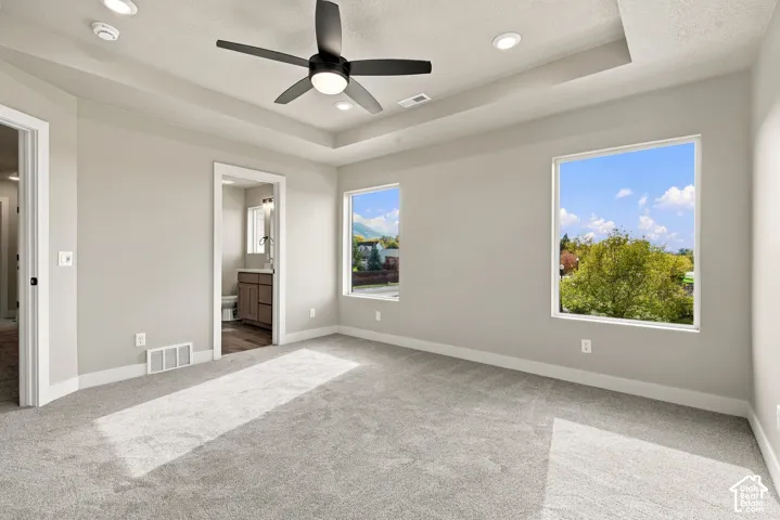 Room featuring a tray ceiling, recessed lighting, matte black ceiling fan, neutral carpeting, and large windows