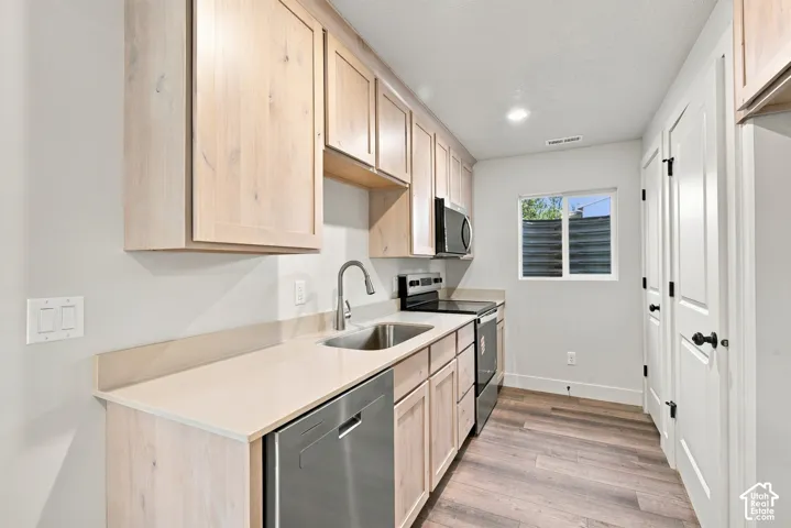 Kitchen featuring light wood-finish cabinetry, solid-surface countertops, stainless steel appliances, and wood-finish flooring