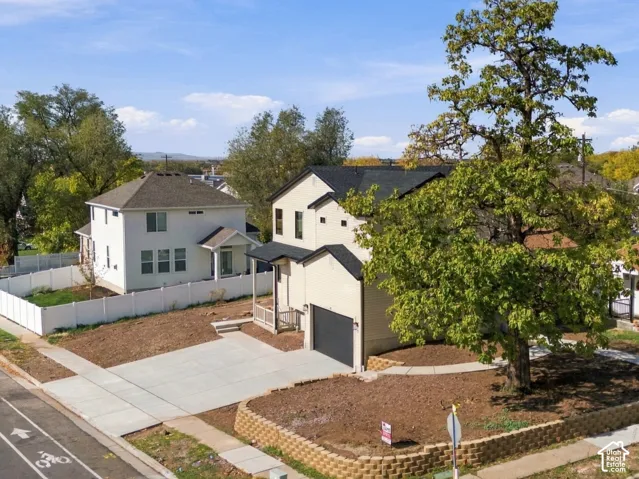 Two-story exterior featuring a light-colored facade, a dark-toned roof, an attached garage, and a masonry retaining wall enclosing a corner lot