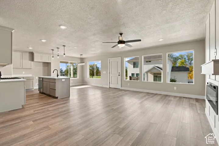 Open-concept space featuring wood-finish flooring, a kitchen island with a matte black faucet, recessed lighting, a ceiling fan, and a built-in electric fireplace
