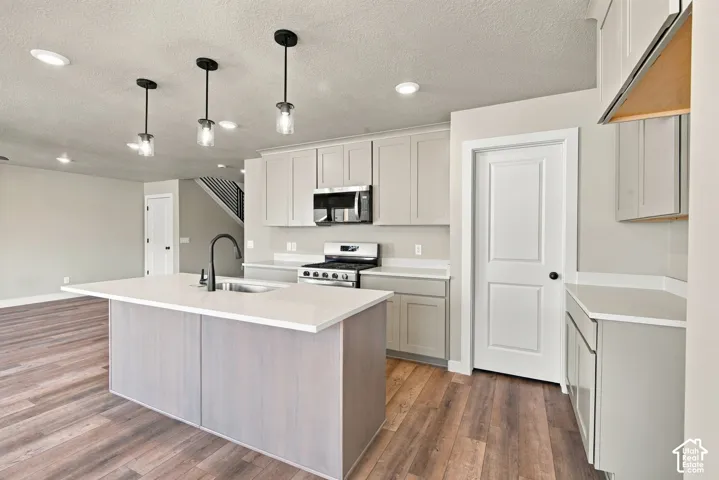 Kitchen featuring light-toned cabinetry, quartz countertops, a central island with an undermount sink and matte black faucet, and wood-finish flooring