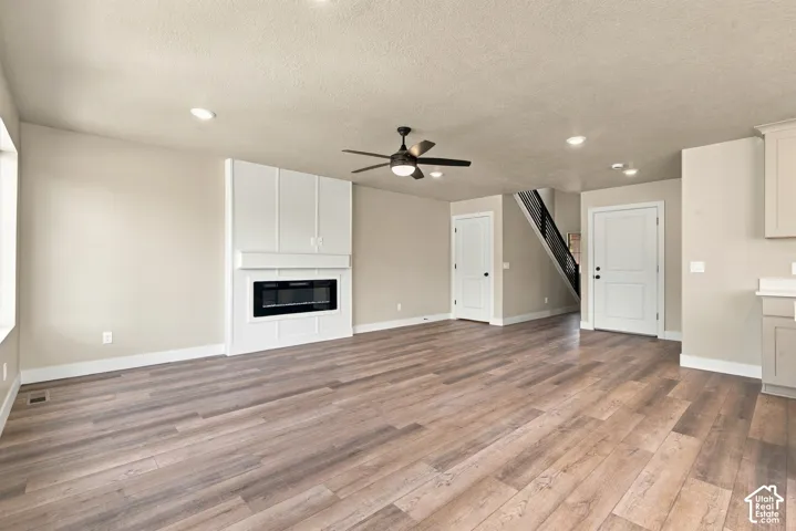Living area featuring wood-finish flooring, a wall-mounted electric fireplace with custom millwork surround, recessed lighting, and a ceiling fan with integrated lighting